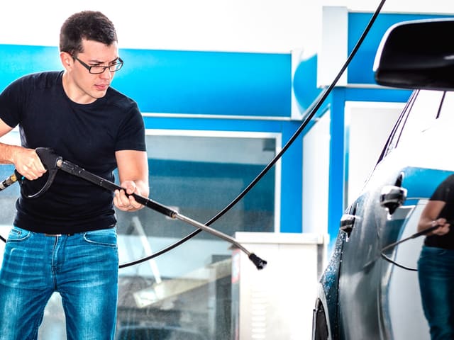Hombre lavando auto con manguera en autolavado