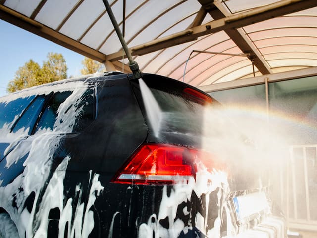 Auto negro lavándose a presión bajo techo