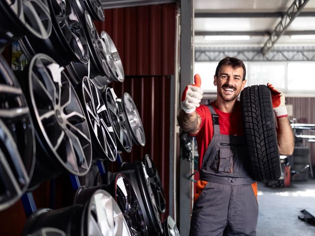 Mecánico sonriente con rueda en taller de llantas